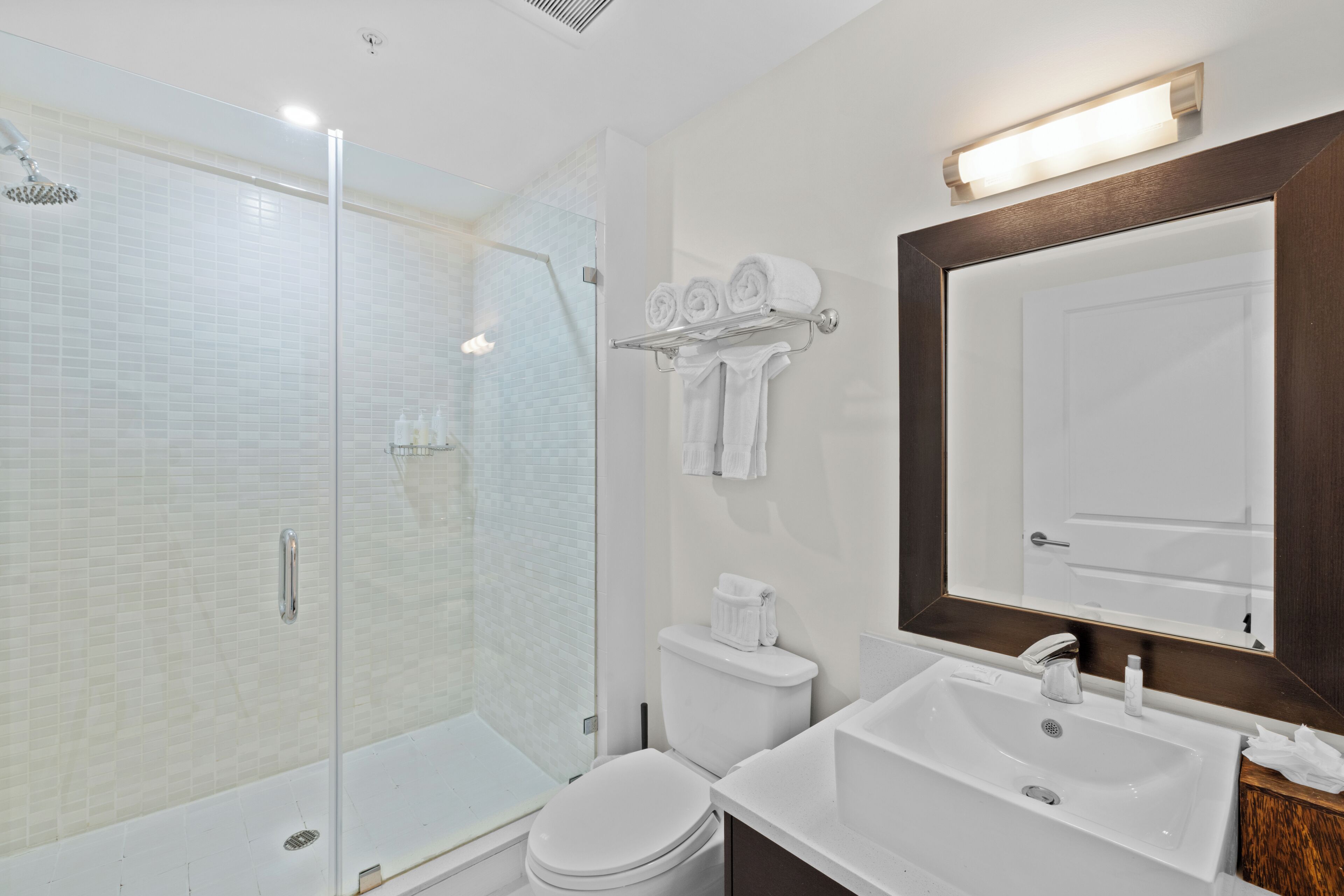 Une salle de bain moderne avec une douche à parois de verre, des toilettes blanches, un lavabo et un grand miroir.