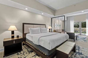 Une chambre d’hôtel avec un grand lit, deux tables de chevet avec des lampes, un banc et une vue sur un jardin, visible à travers une porte vitrée.
