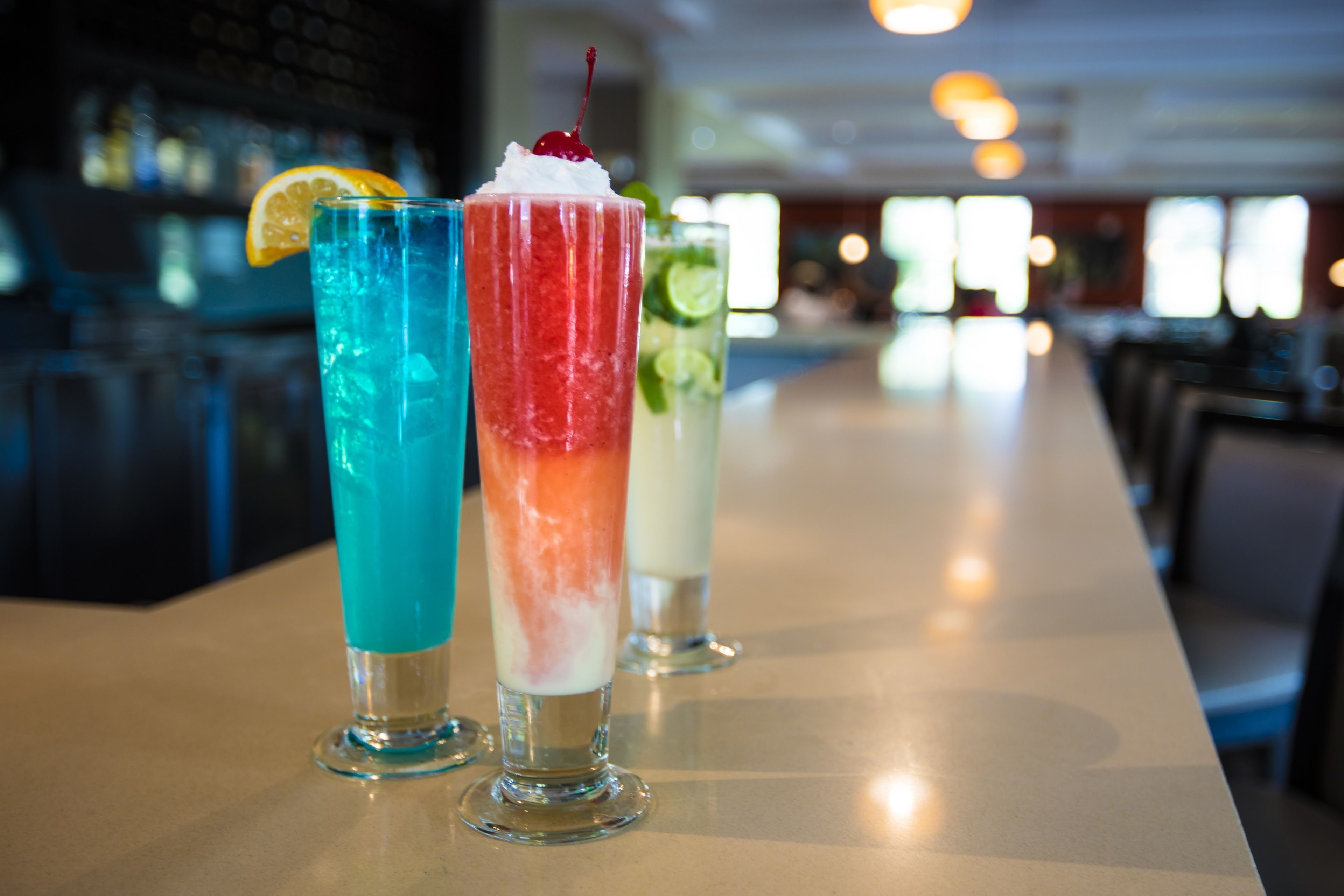 Three colorful drinks on a bar counter in a restaurant.