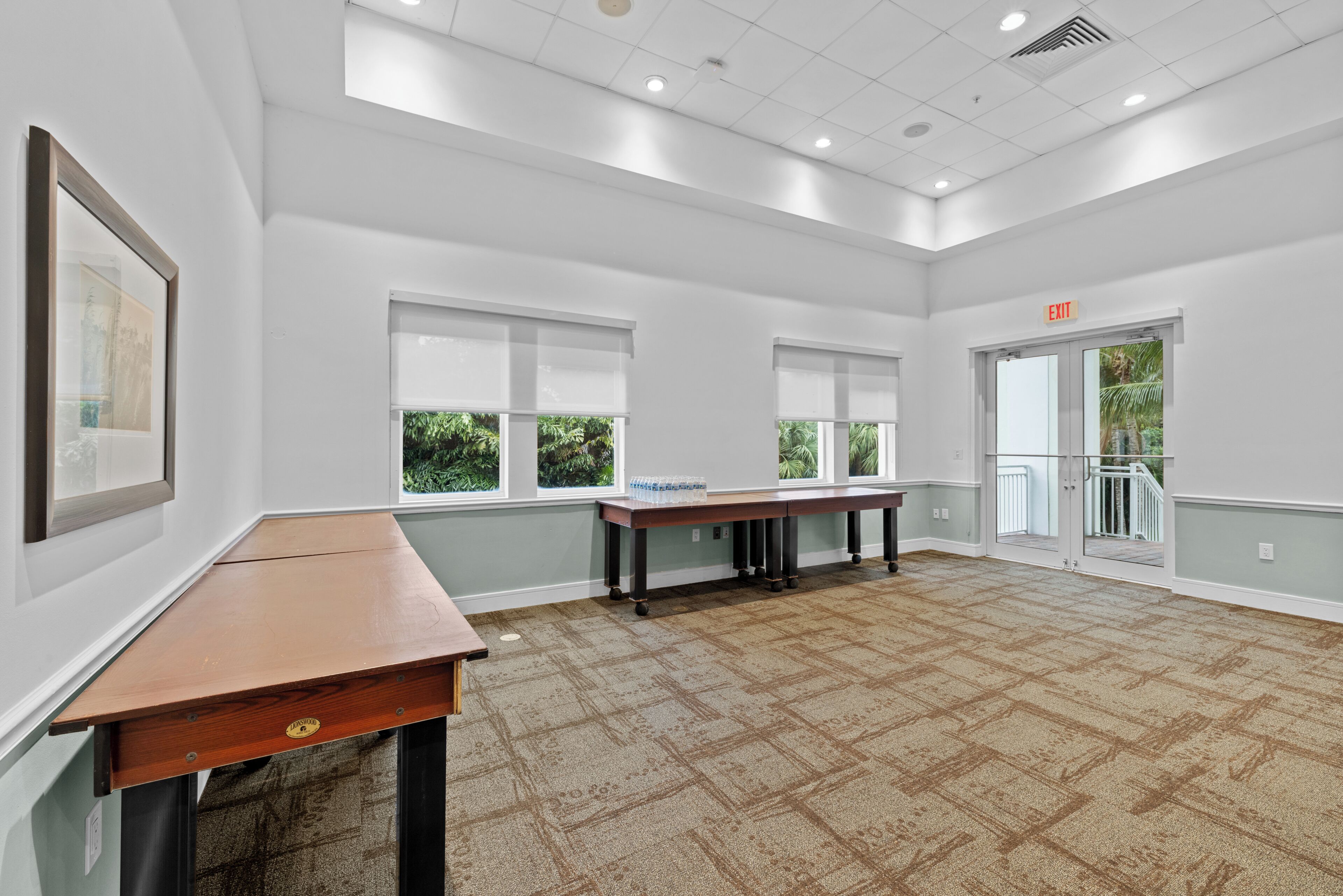 A spacious room with a large table, windows, and an exit sign.