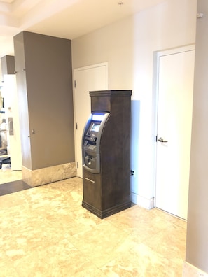 En mörkfärgad bankomat placerad i en korridor med marmorgolv och vita dörrar.