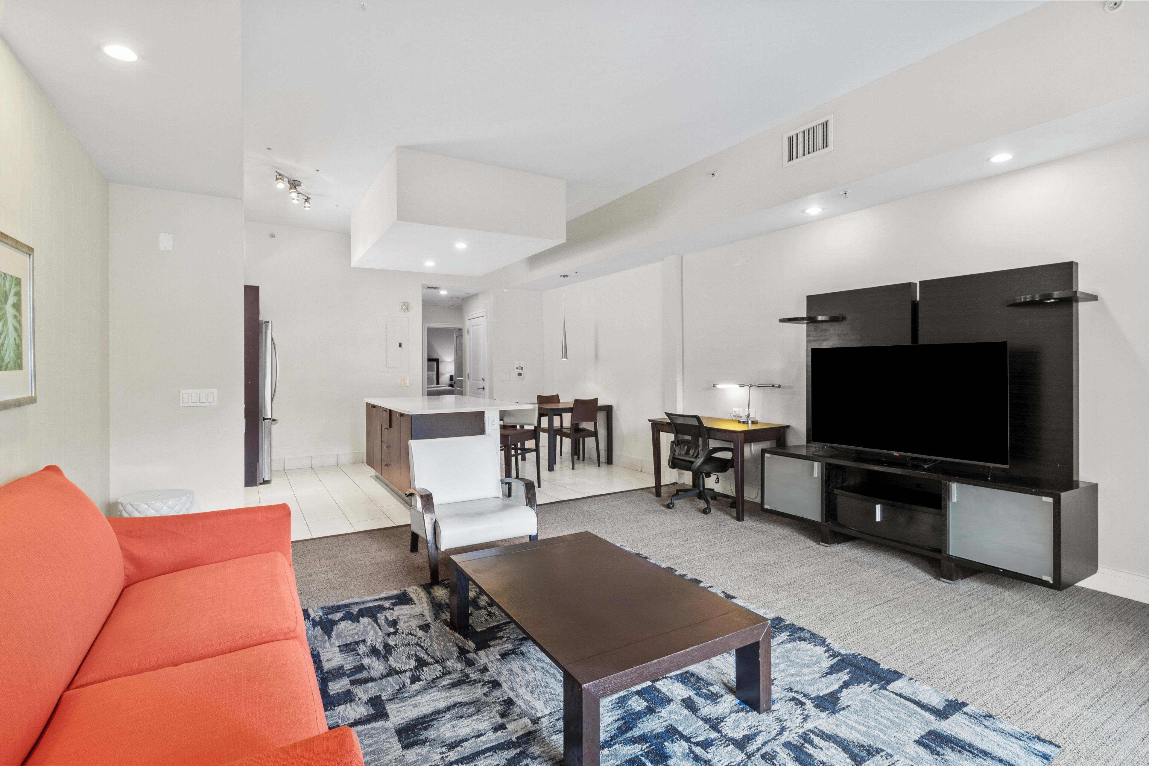 A modern living room with a sofa, a coffee table, a TV, and a kitchen area in the background.