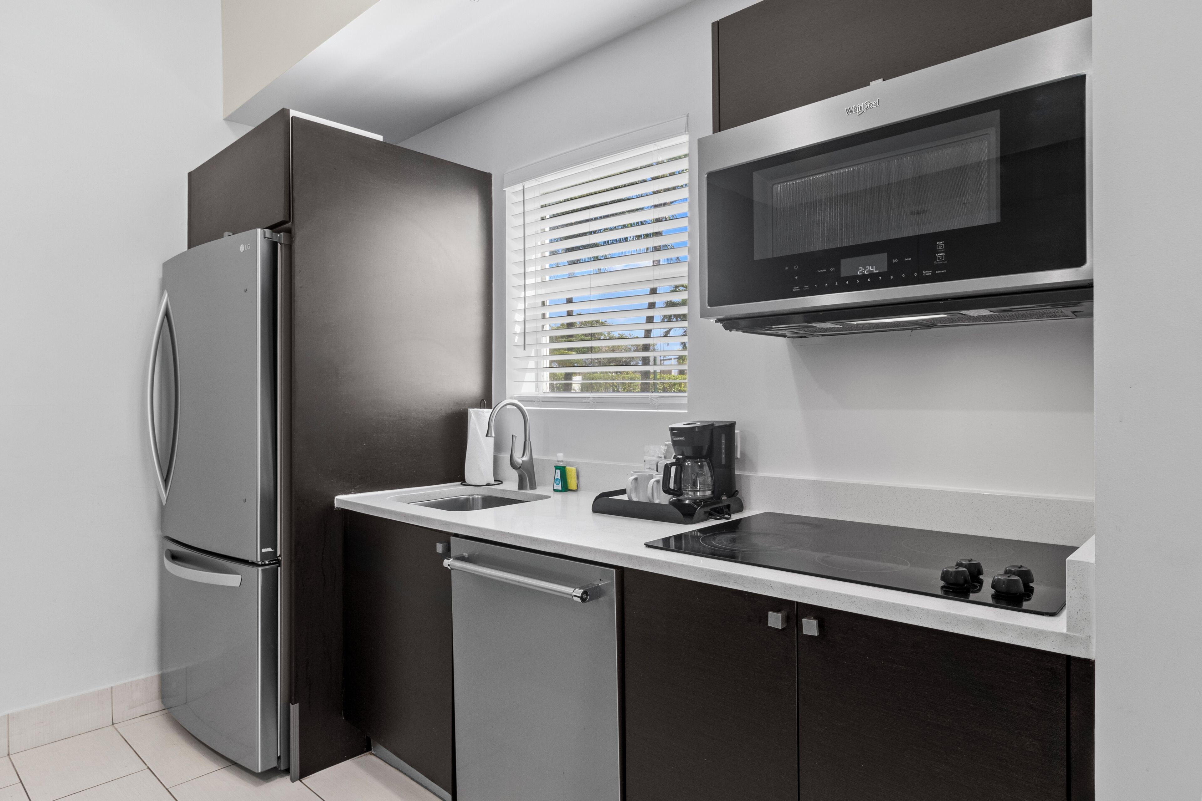 Una cocina moderna con un refrigerador de acero inoxidable, microondas integrado, un lavamanos y una cafetera.