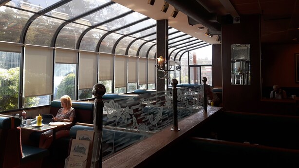 A restaurant with a high, curved glass ceiling allowing natural light, seating with a view, and a decorative metal sculpture on the counter. - Fuller Lake Motel (Chemainus)
