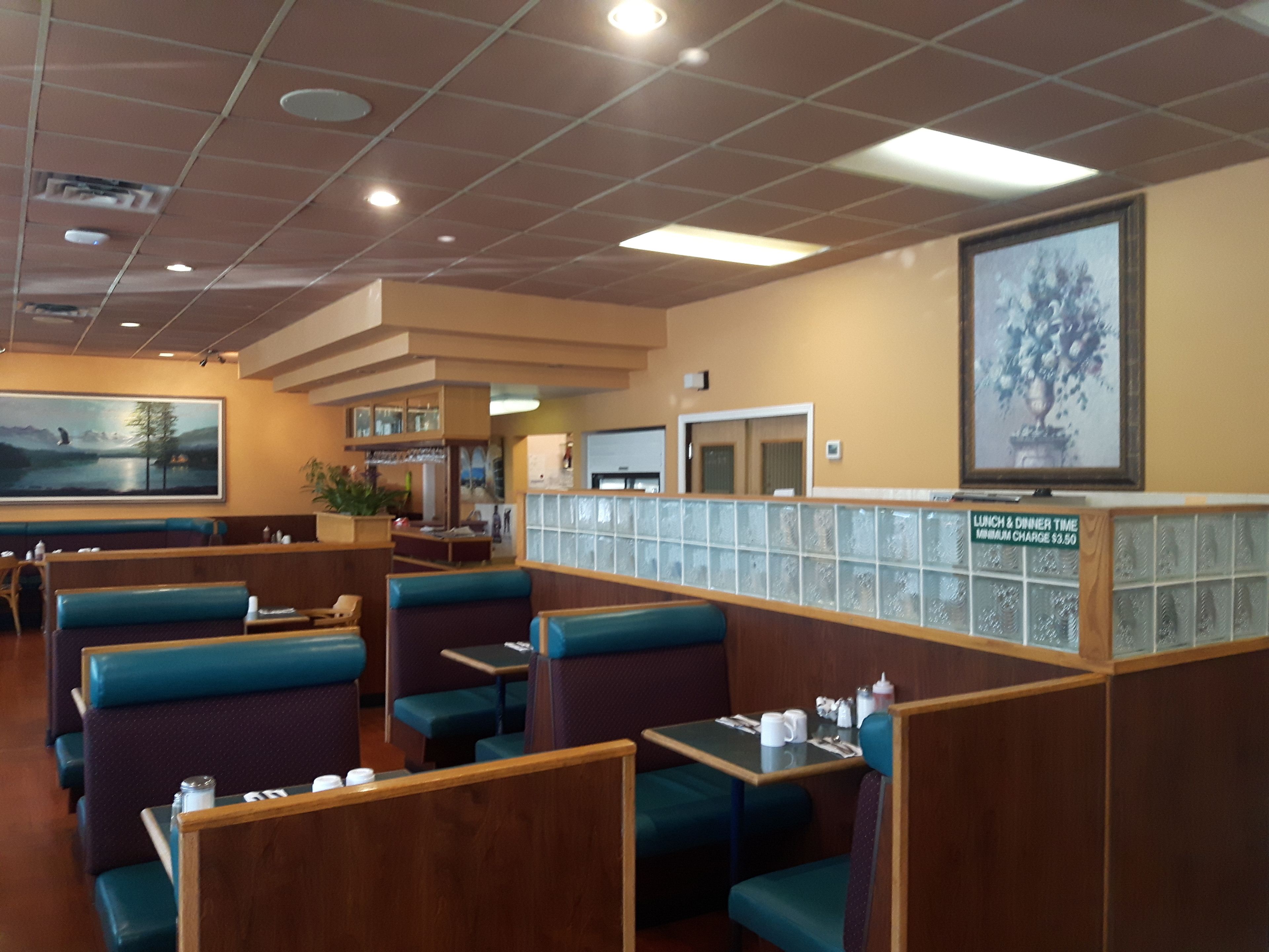 Een restaurant met zitbankjes, een groot schilderij aan de muur en een menubord waarop lunch- en dineruren staan aangegeven.