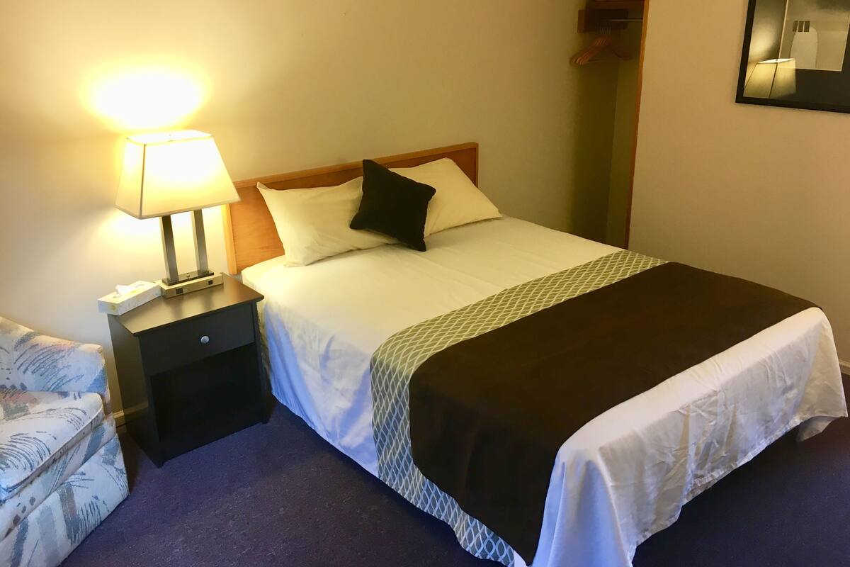 A neatly made bed with a white and black bedspread, a bedside lamp, and a small nightstand with a tissue box.