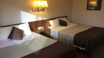 Una habitación de hotel con dos camas individuales, una mesita de noche con lámpara y un cuadro en la pared.