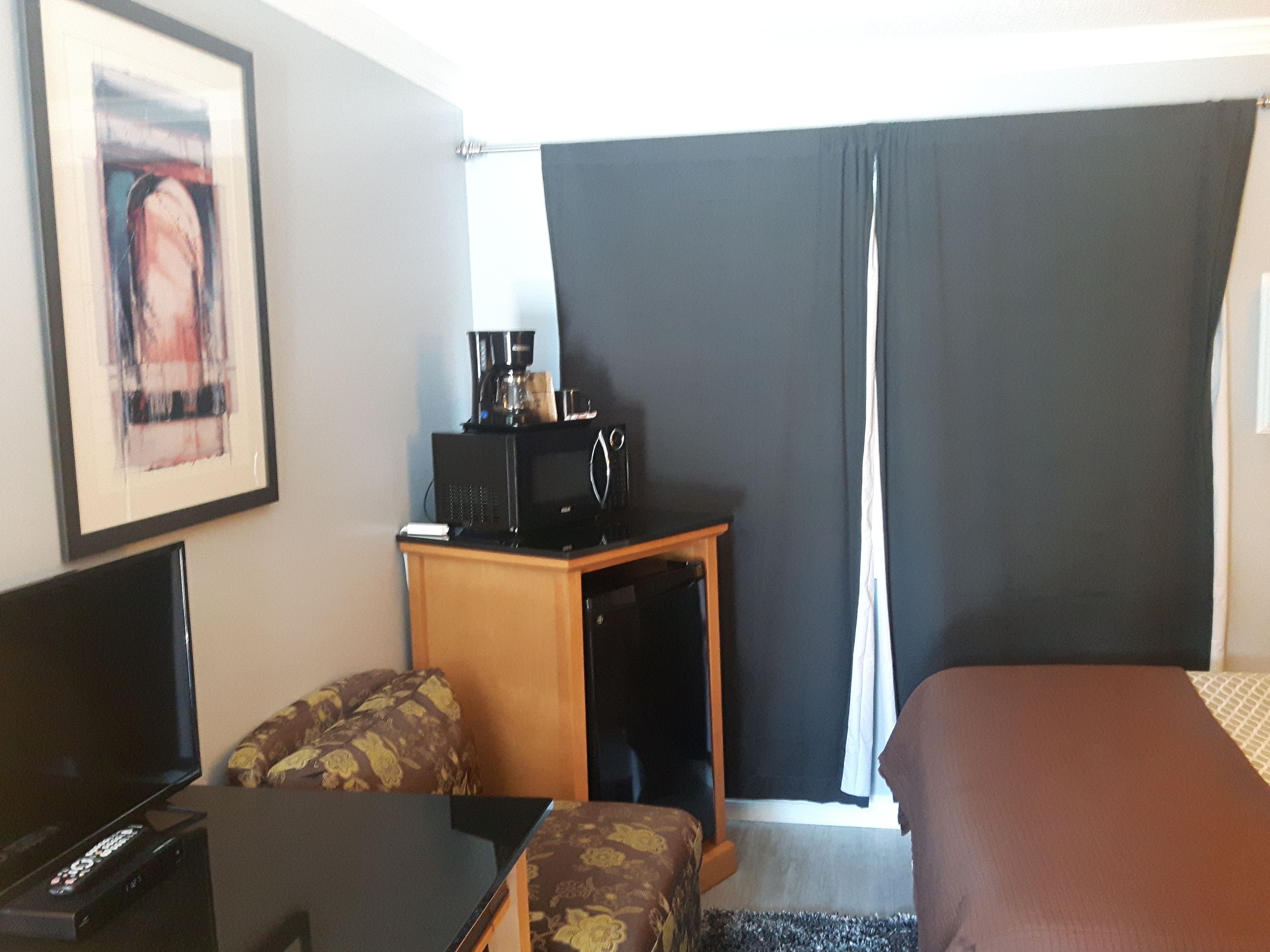 Una habitación de hotel con cama, escritorio, computadora, cafetera y televisor.