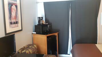Una habitación de hotel con cama, escritorio, computadora, cafetera y televisor.