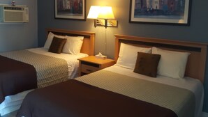 A hotel room with two beds, a nightstand with a lamp, and two framed pictures on the wall. - Fuller Lake Motel (Chemainus)