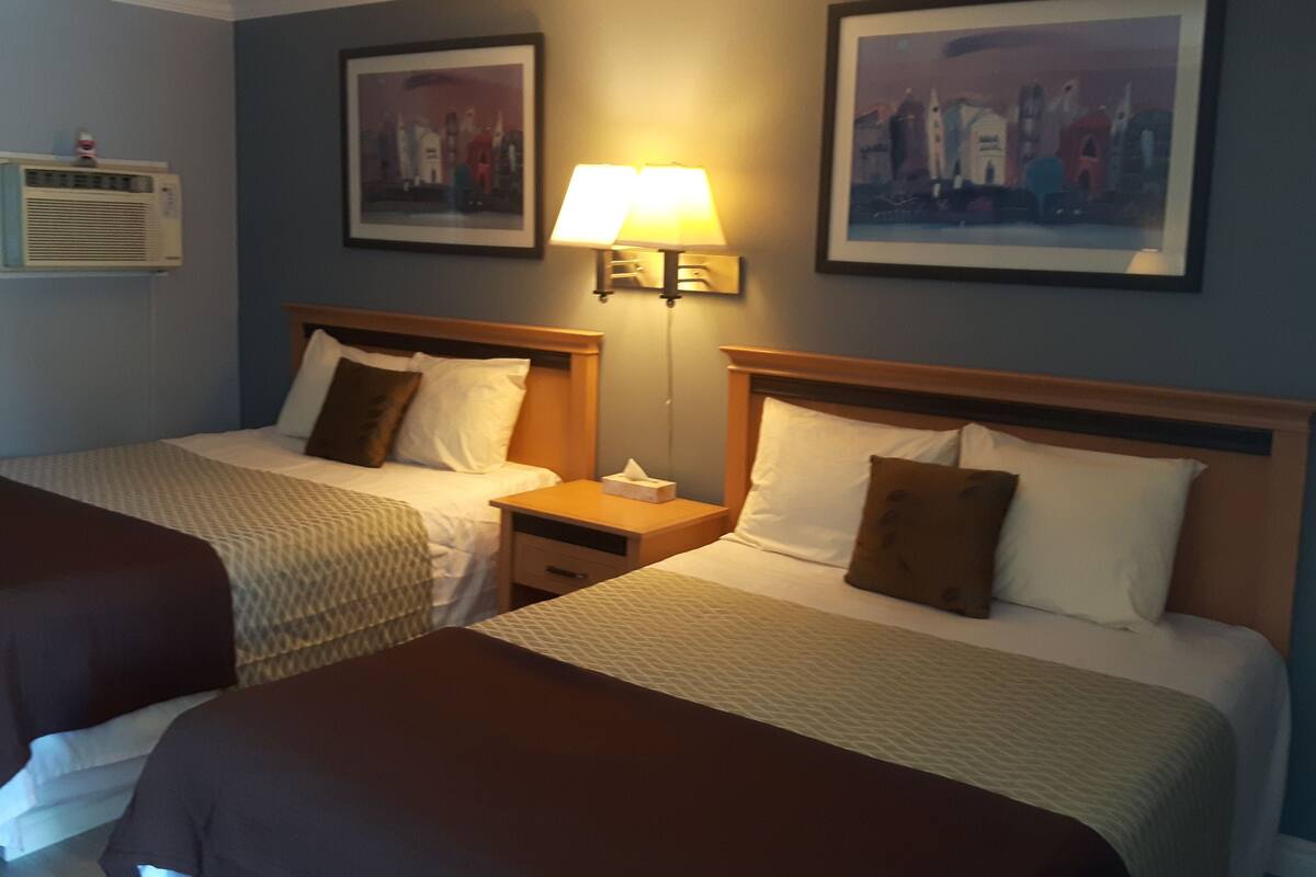 A hotel room with two beds, a nightstand with a lamp, and two framed pictures on the wall.