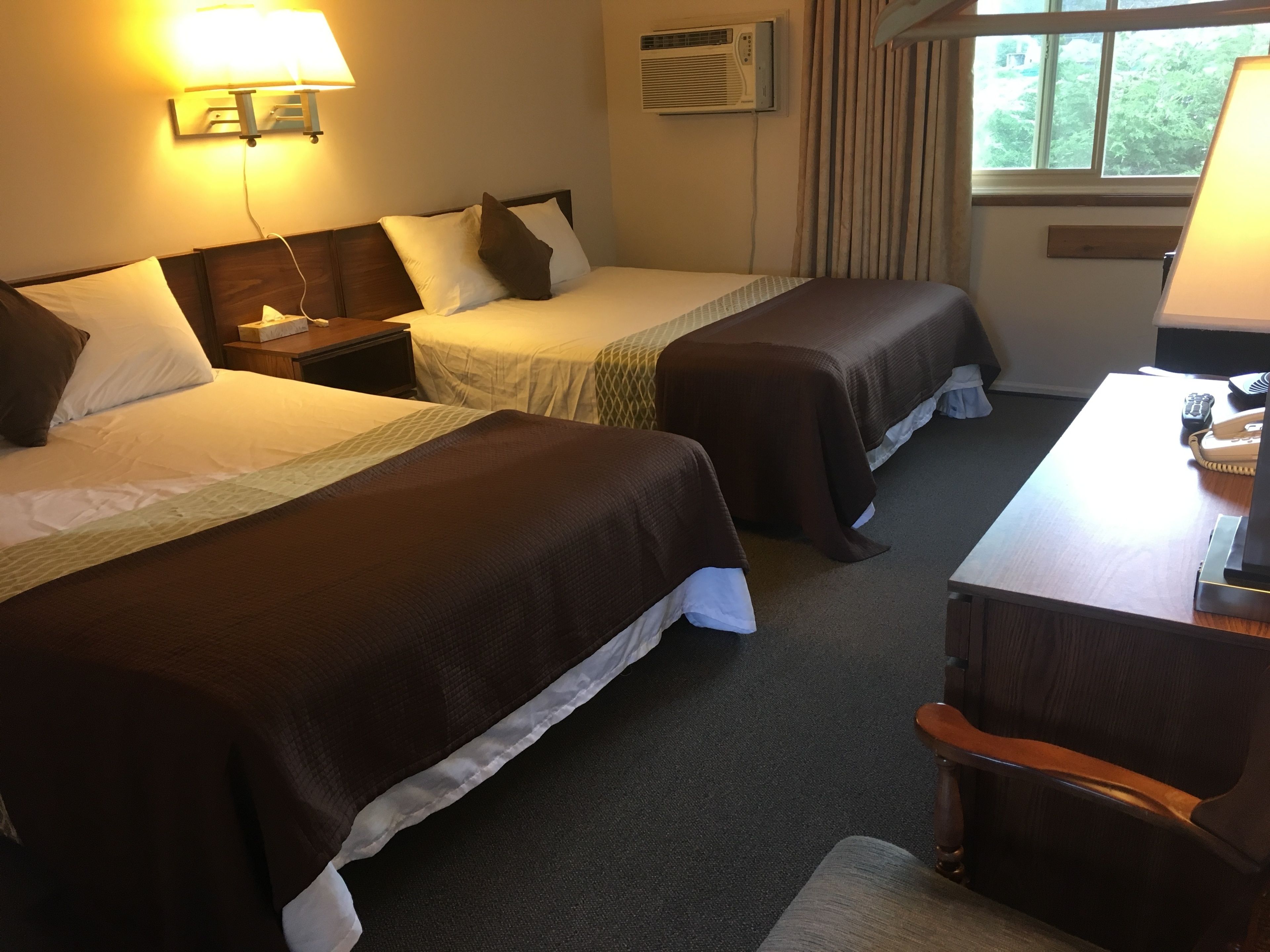 A hotel room with two beds, a desk with a telephone, and an air conditioning unit on the wall.