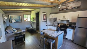 A compact kitchen with a central island, a dining area with a sofa, and a ceiling fan. - Fuller Lake Motel (Chemainus)