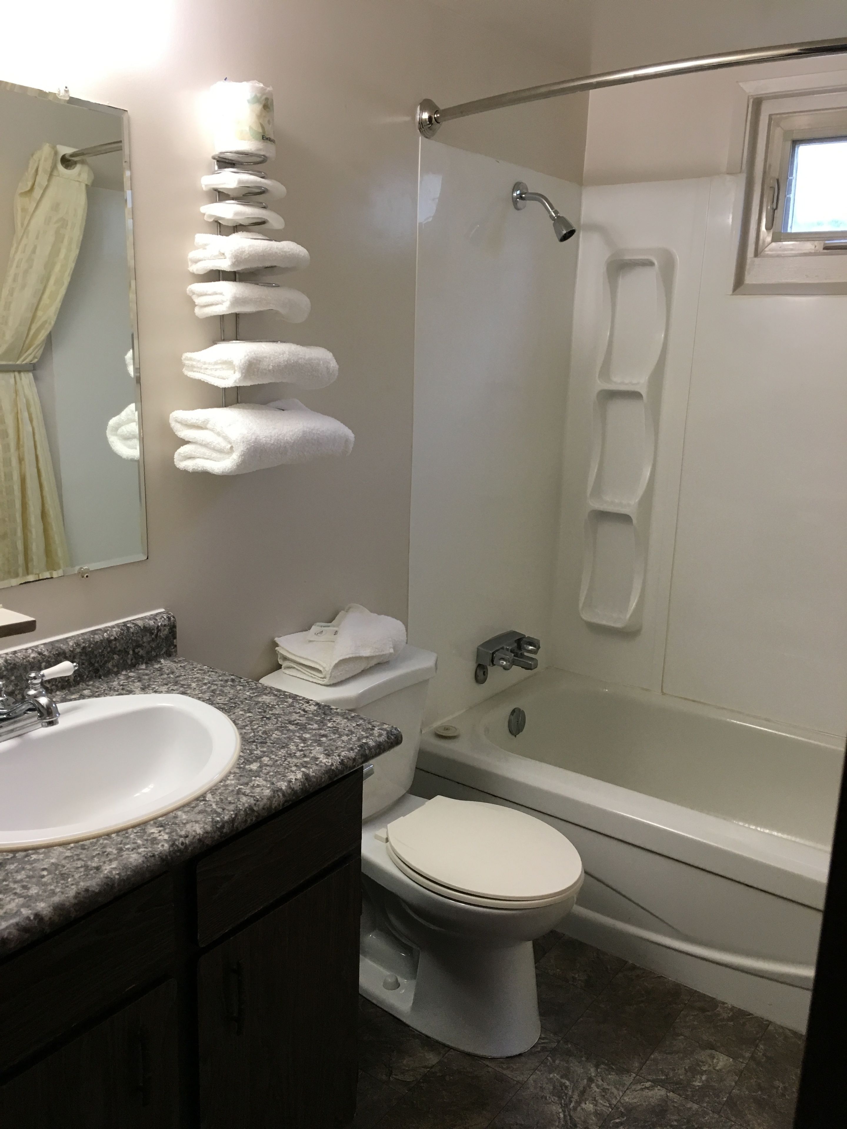 Un baño con lavamanos, inodoro y bañera. Hay un perchero con varias toallas.