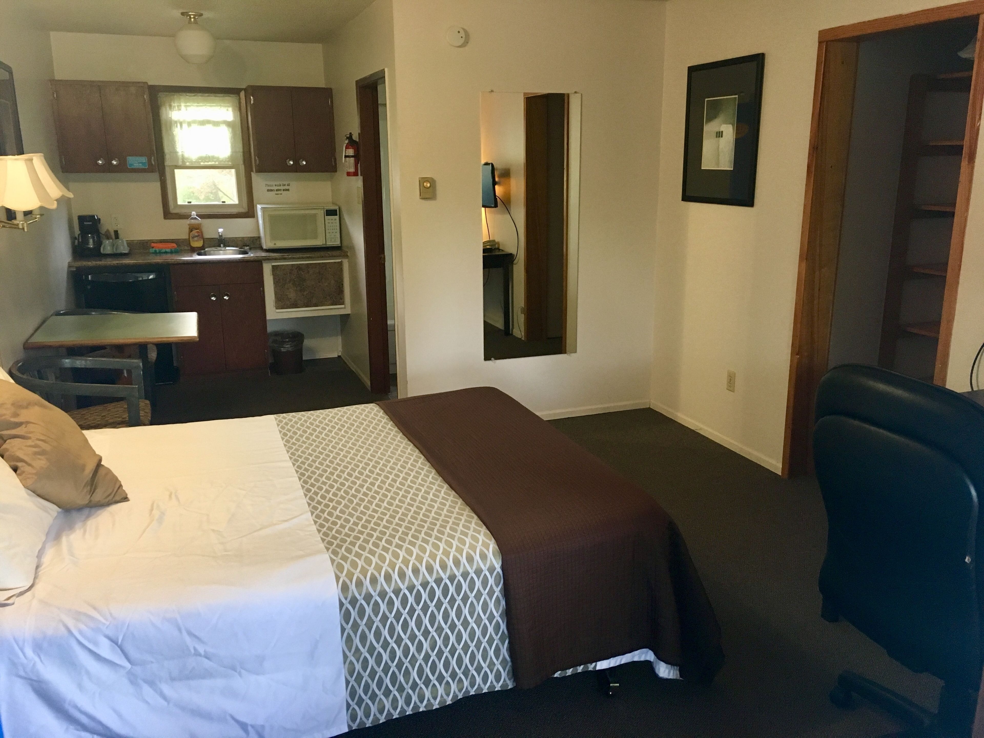 A hotel room with a bed, a desk, a chair, a kitchenette, and a bathroom.