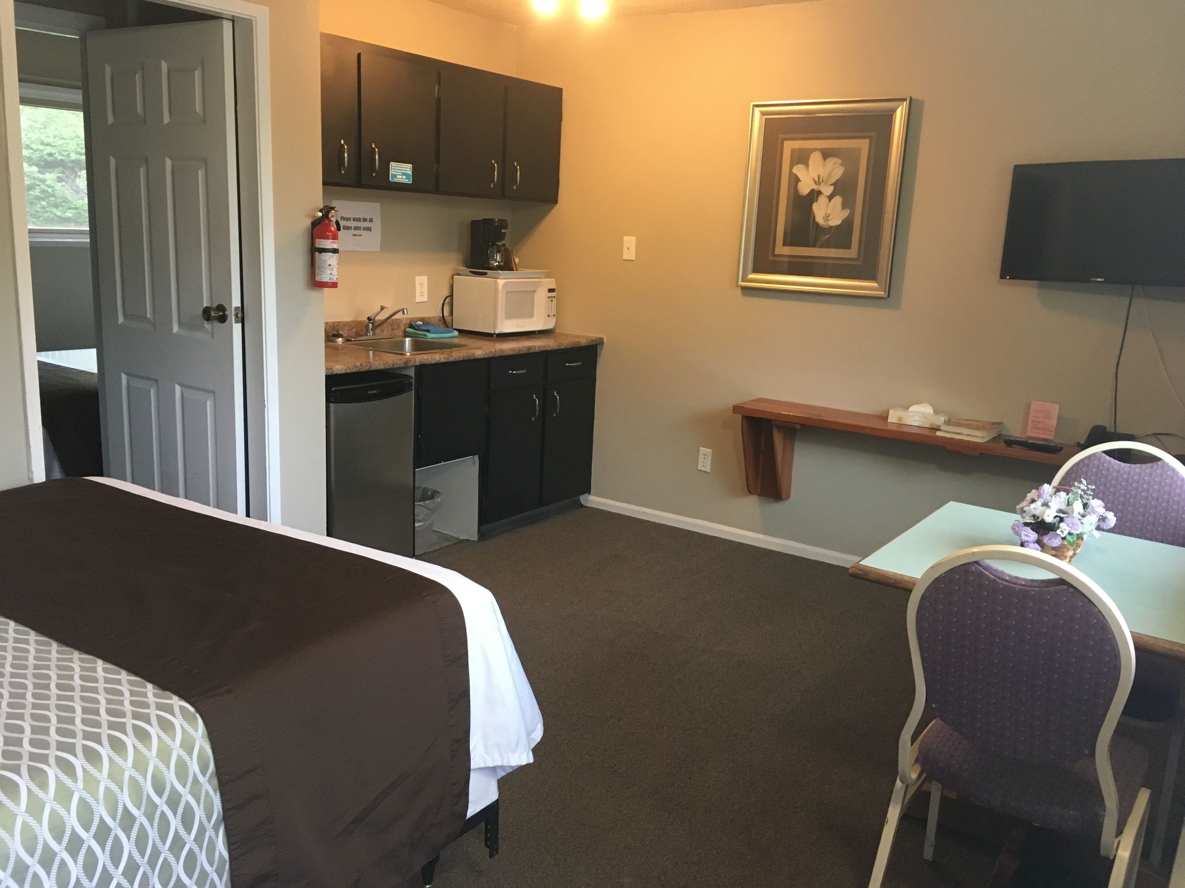 Habitación de hotel con cama, escritorio, silla, microondas, lavabo, armarios y televisor.