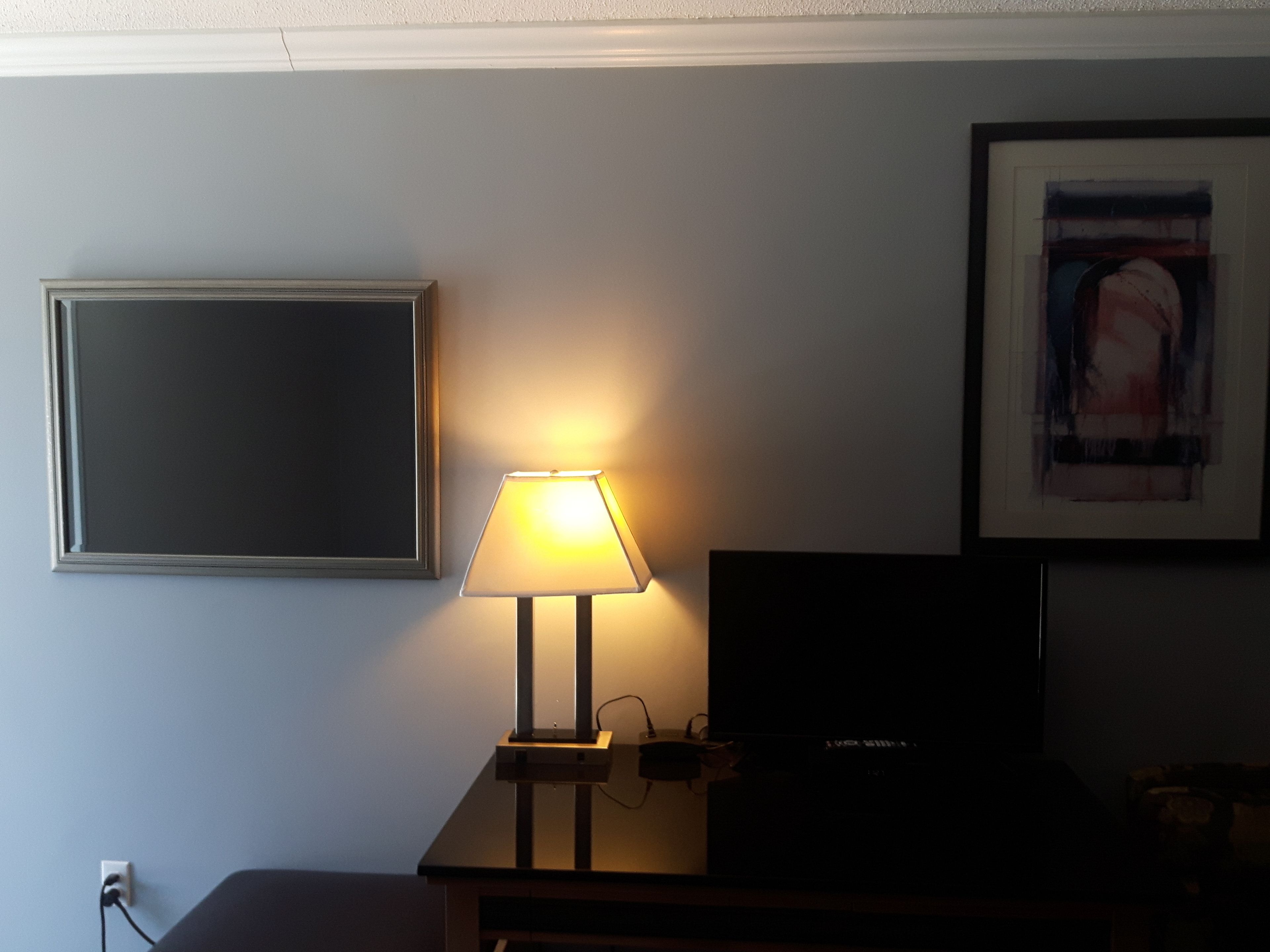 Quarto com escrivaninha, luminária, quadro e televisão.