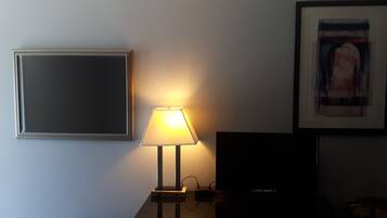 Quarto com escrivaninha, luminária, quadro e televisão.