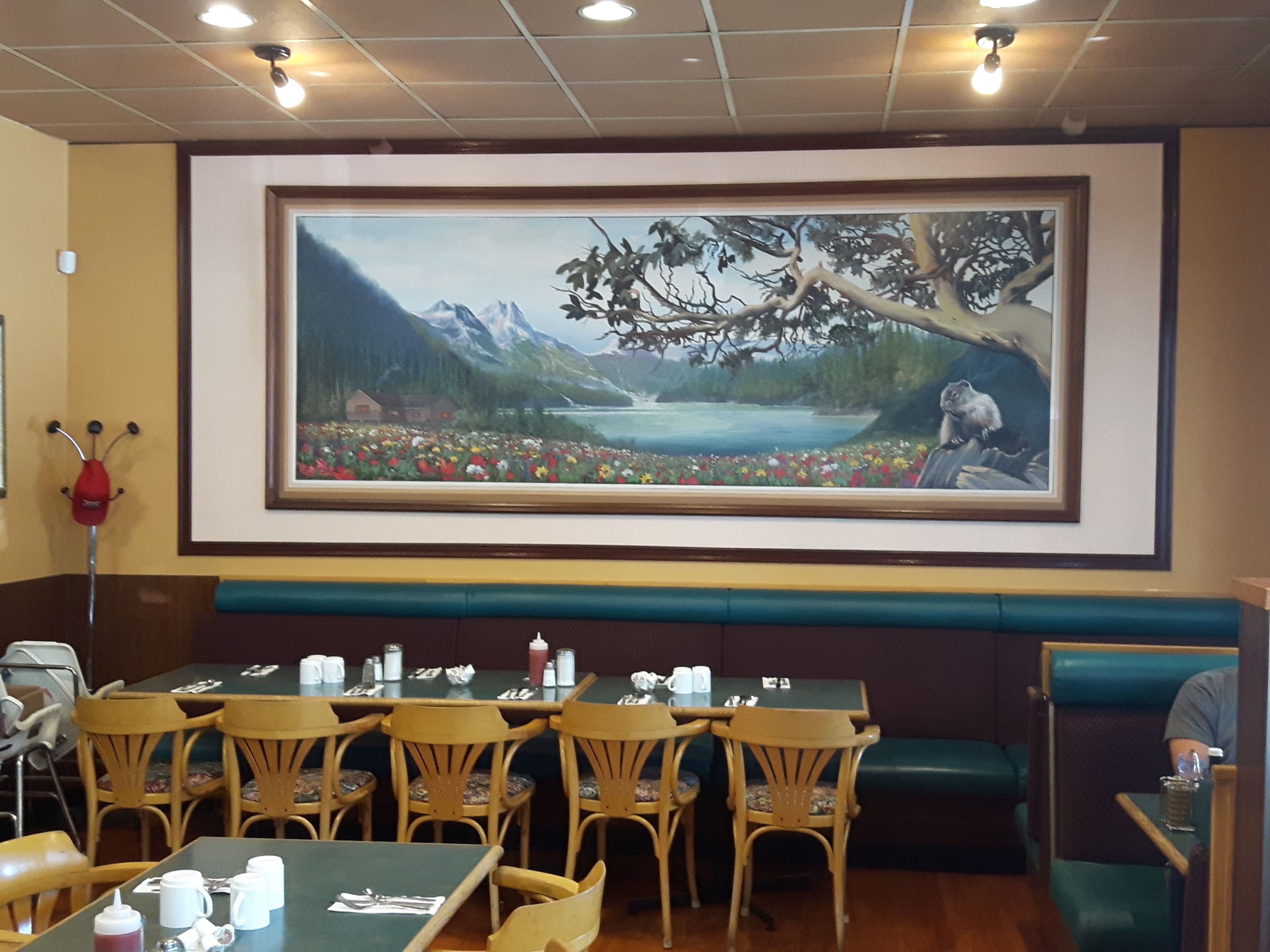 A restaurant with wooden chairs, tables, and a large painting of a mountain landscape on the wall.