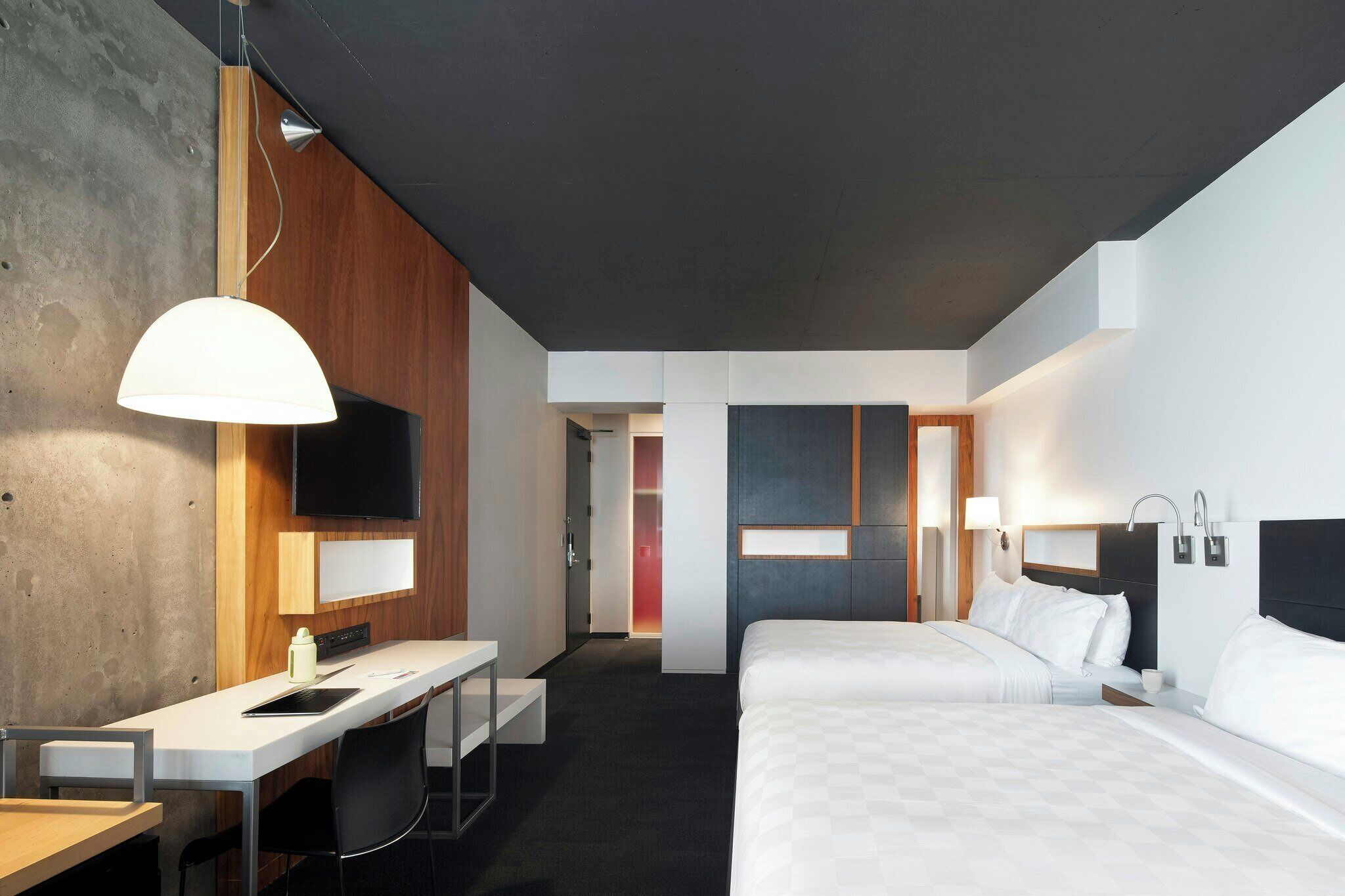A modern hotel room with a desk, two beds, a TV, and a bathroom.