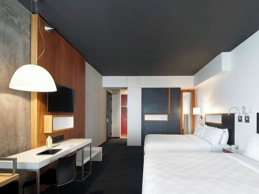 A modern hotel room with a desk, two beds, a TV, and a bathroom.