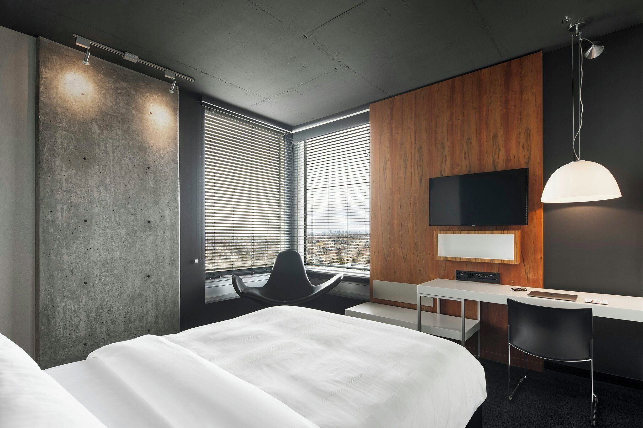 A hotel room with a bed, a desk, a chair, a TV, and a window with blinds.