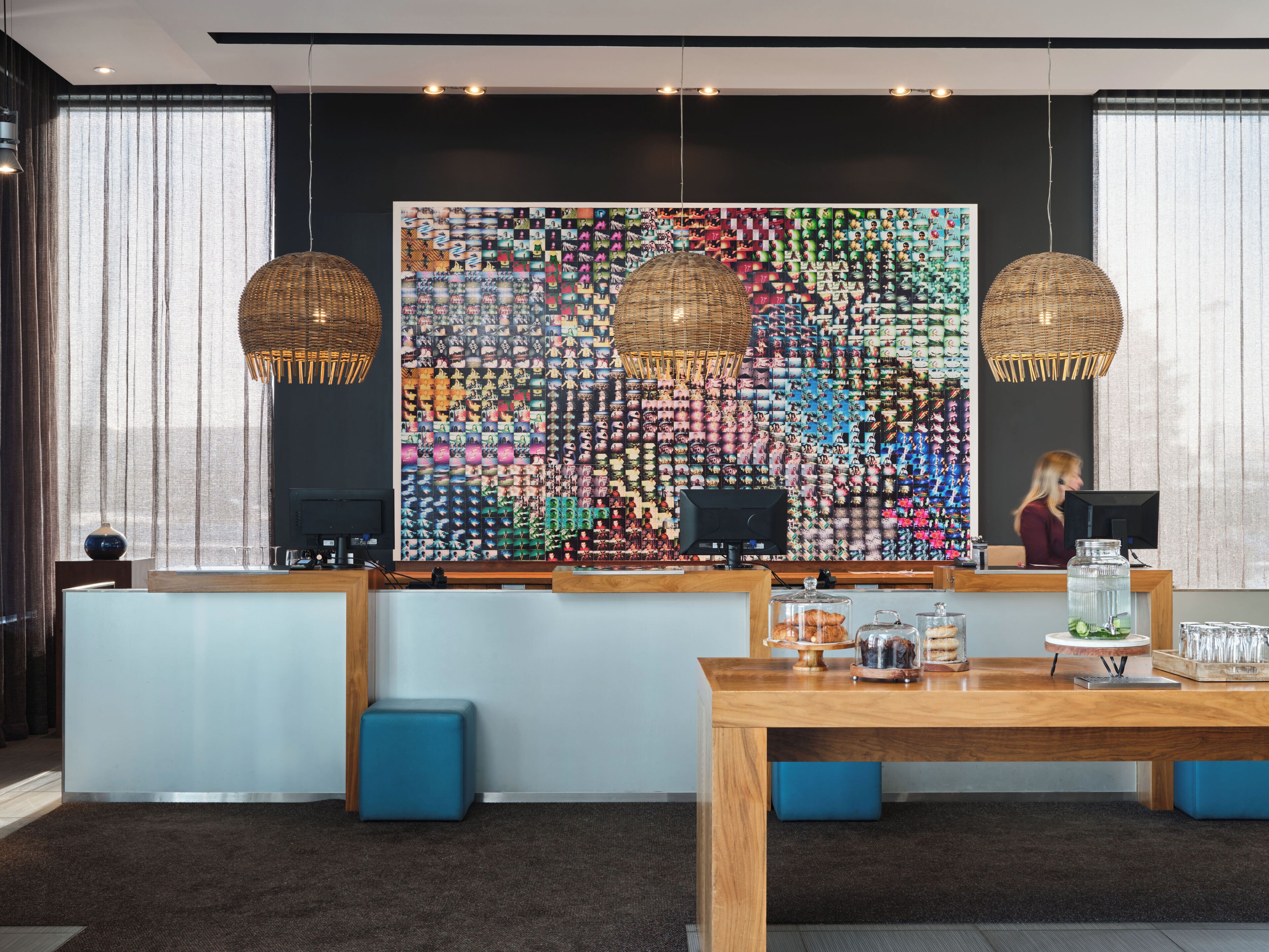 Un moderno vestíbulo de hotel con una gran instalación artística en la pared, una recepción y una mesa de madera con asientos.