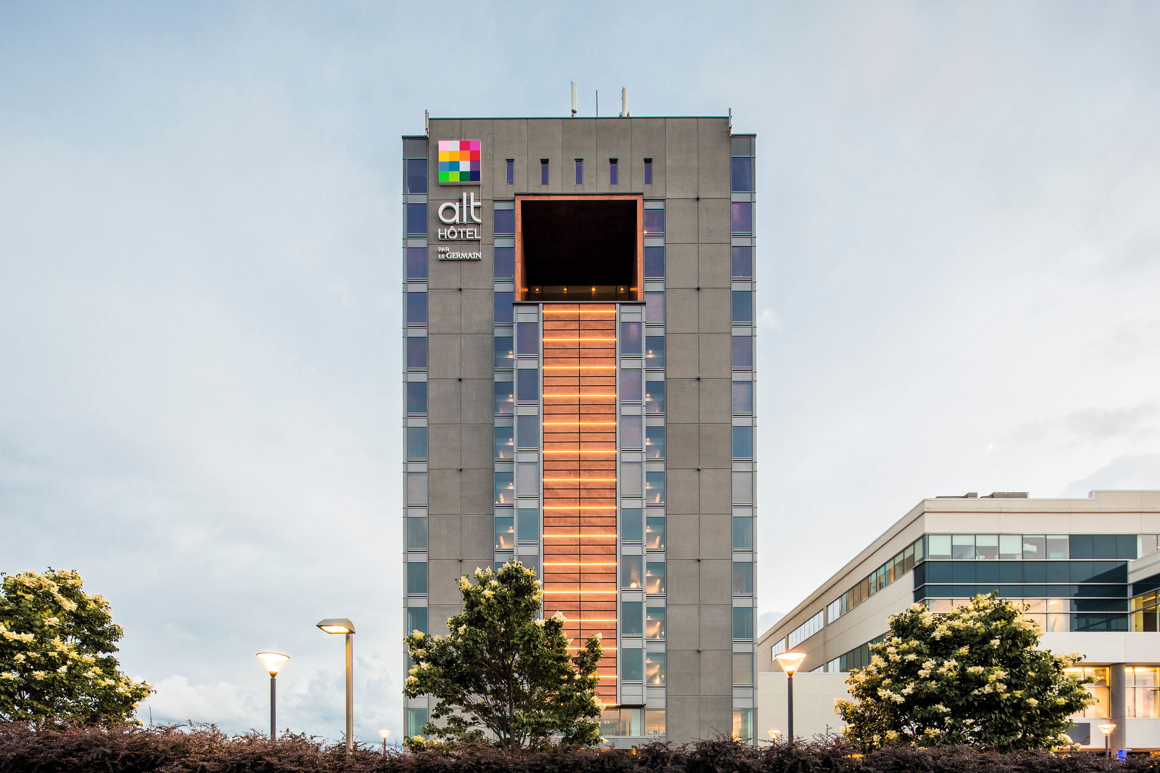 A modern hotel building with a prominent logo, a central entrance, and a clear sky.