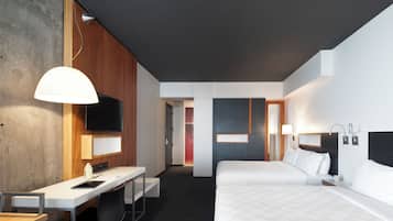 A modern hotel room with a desk, two beds, a TV, and a bathroom visible through an open door.