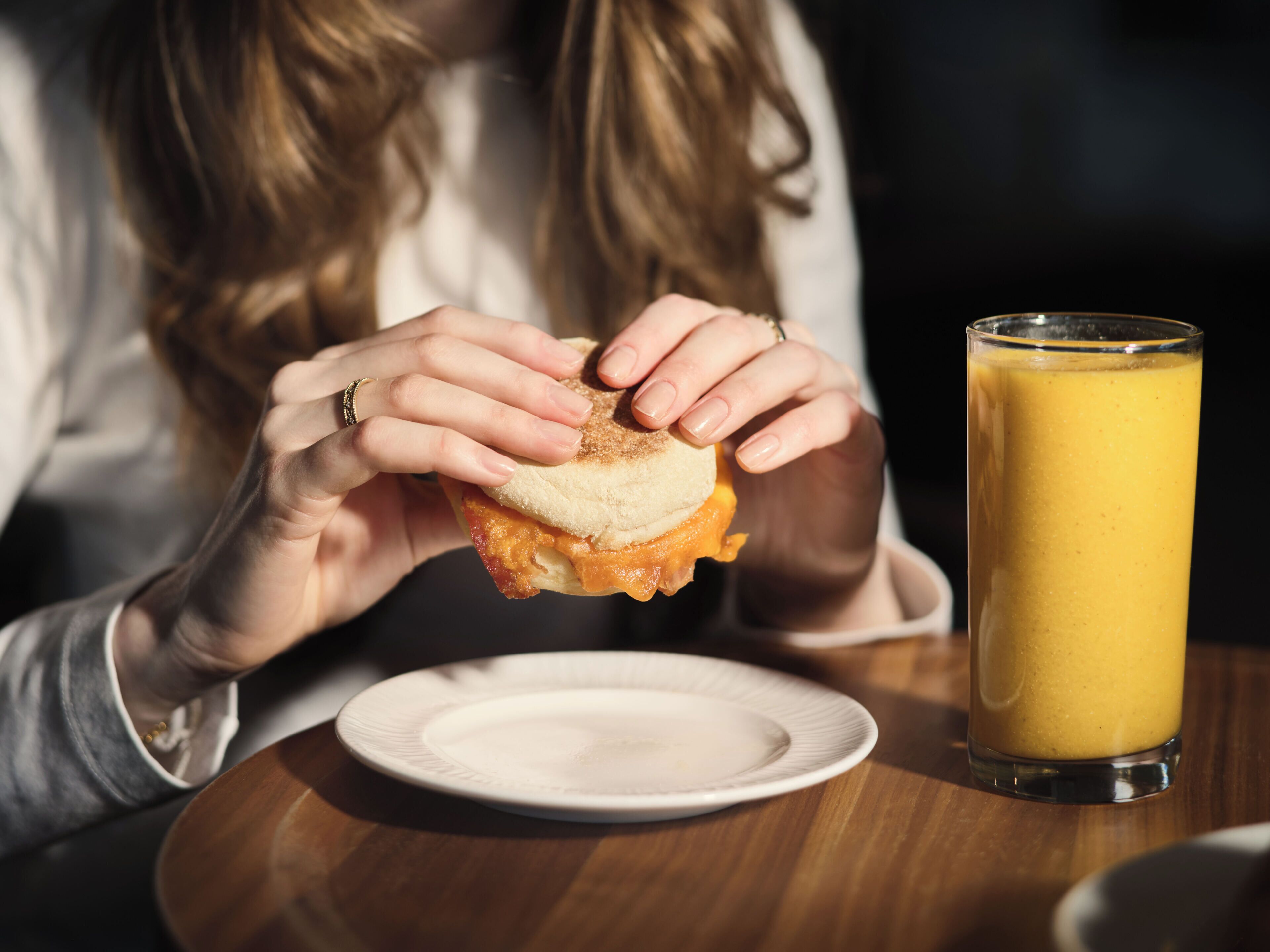 A person holding a sandwich with a glass of orange juice on a table.