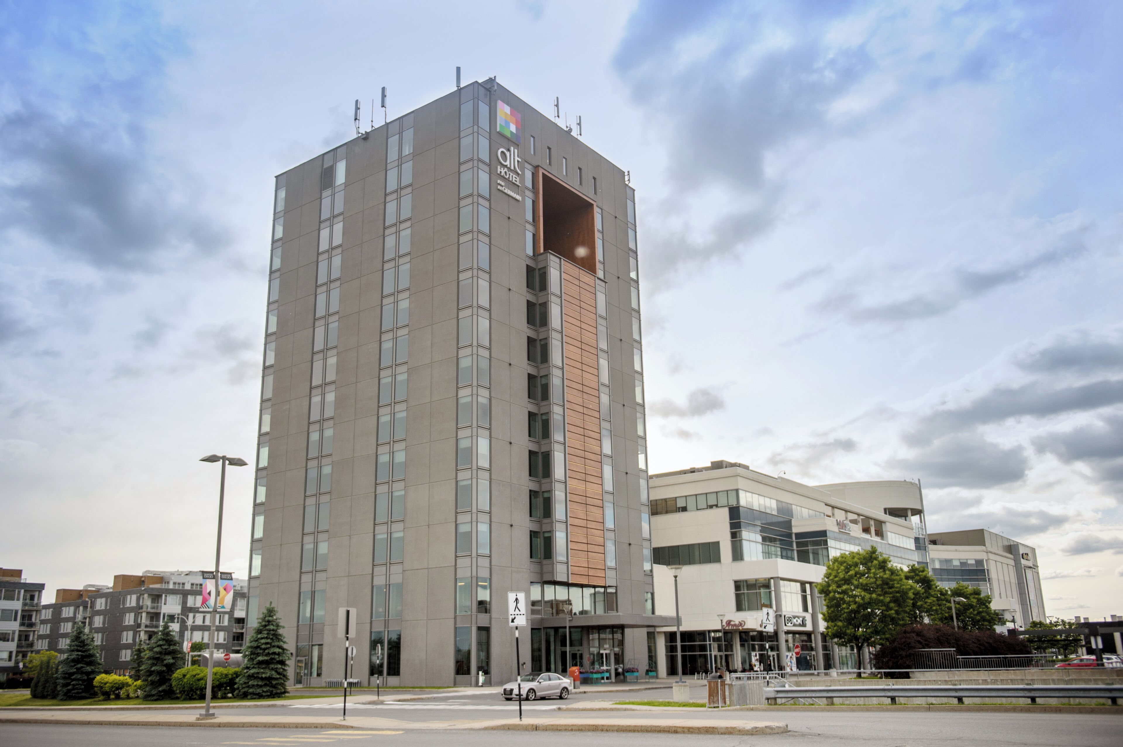 A modern hotel with a prominent entrance, a pedestrian crossing, and a clear sky.