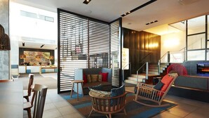 A modern living room with a sofa, chairs, and a coffee table. There is a staircase leading to an upper level, and a bookshelf filled with books. - Hôtel Alt Quartier DIX30 (Brossard)