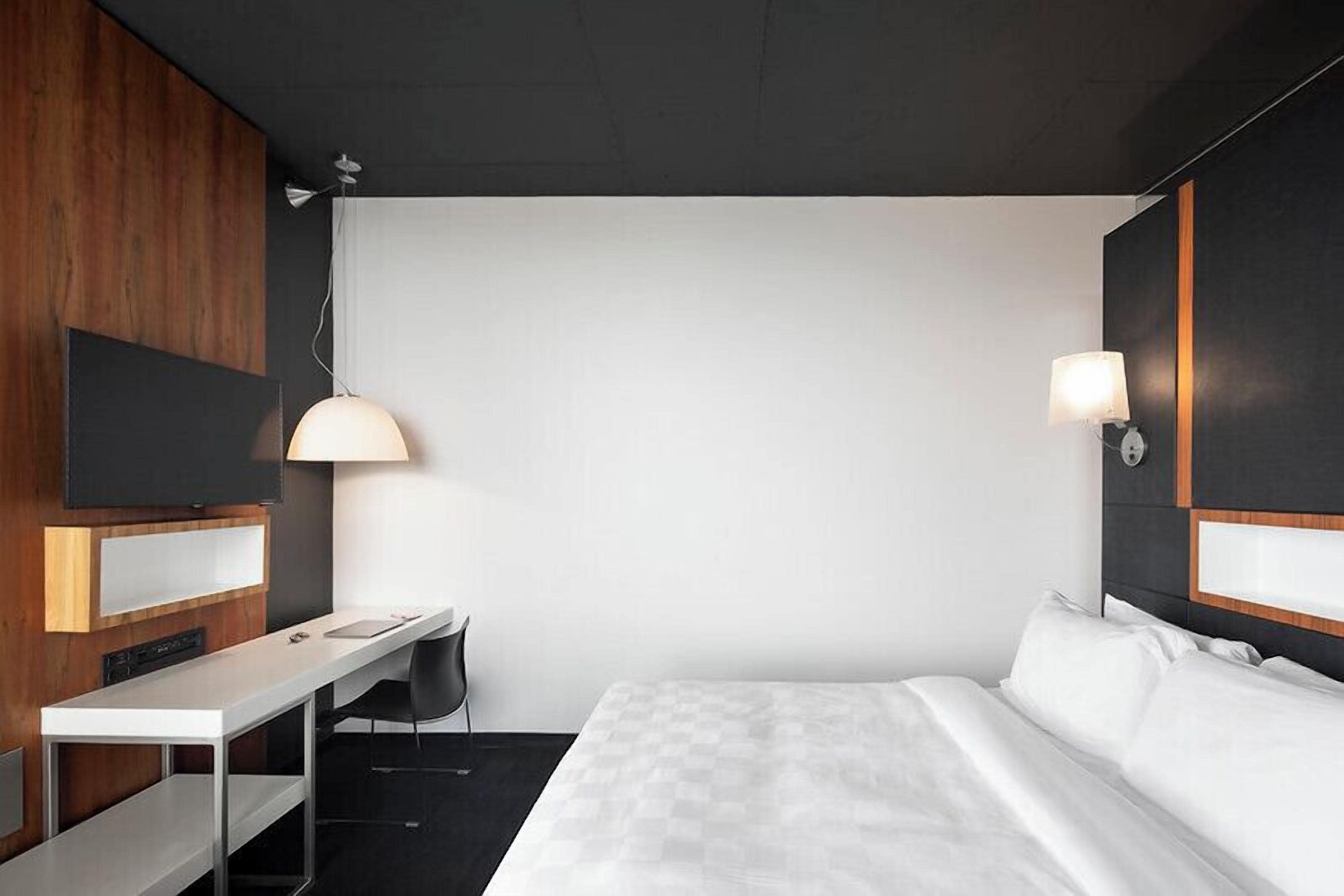 A hotel room with a bed, a desk, a chair, a television, and a lamp.