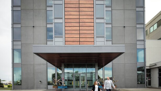 A modern building with a large entrance, glass doors, and a wooden panel accent. - Hôtel Alt Quartier DIX30 (Brossard)