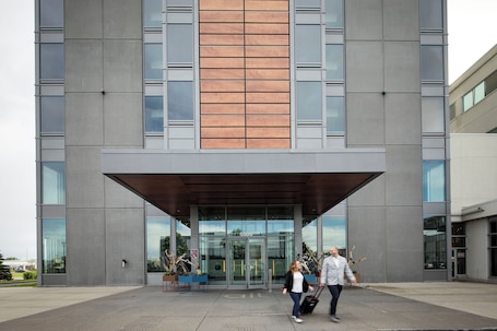 A modern building with a large entrance, glass doors, and a wooden panel accent.