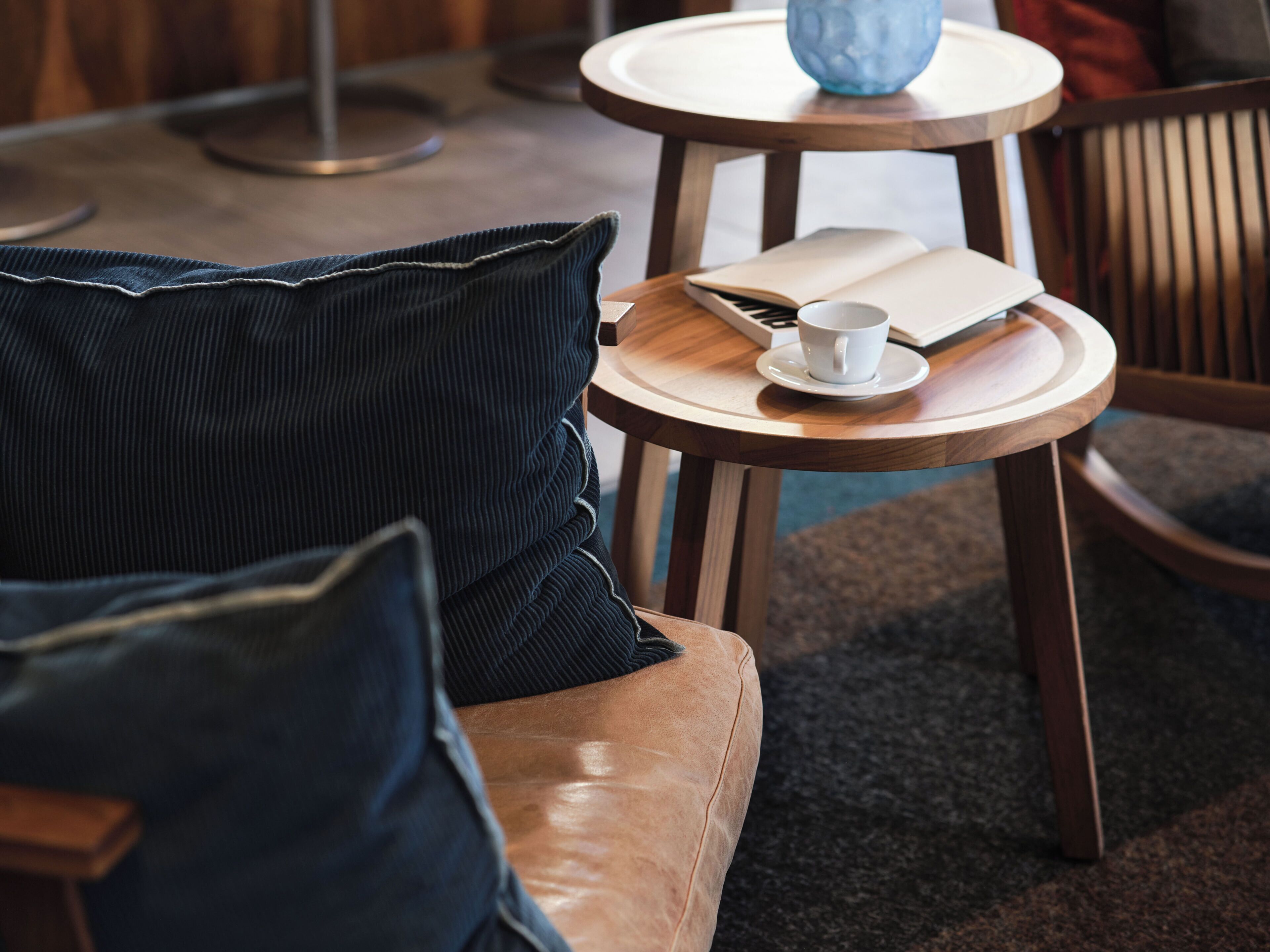 Un sofá de cuero con un cojín oscuro, una mesita de madera con un libro y una taza, y un jarrón azul.