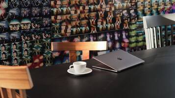 A table with a laptop and a cup, a wooden chair, and a wall with a collage of photos.