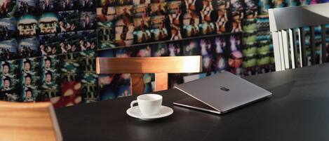 A table with a laptop and a cup, a wooden chair, and a wall with a collage of photos.