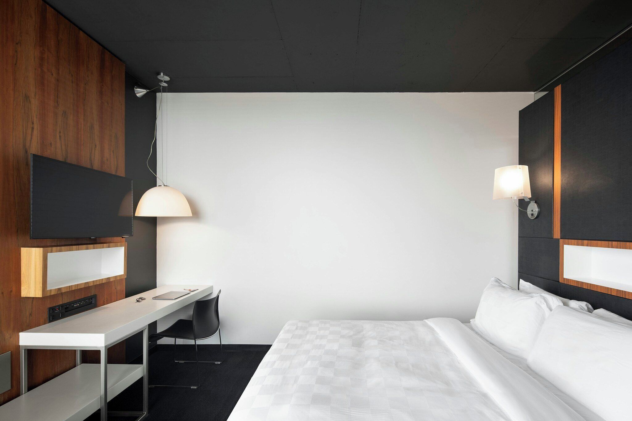 Una habitación de hotel con cama, escritorio, silla, televisor y lámpara.