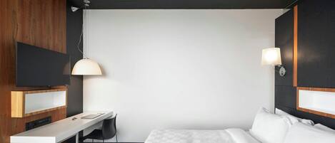A hotel room with a bed, a desk, a chair, a TV, and a lamp.