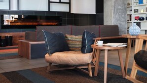 A modern lounge area with a sofa, a wooden table, and a fireplace. - Hôtel Alt Quartier DIX30 (Brossard)
