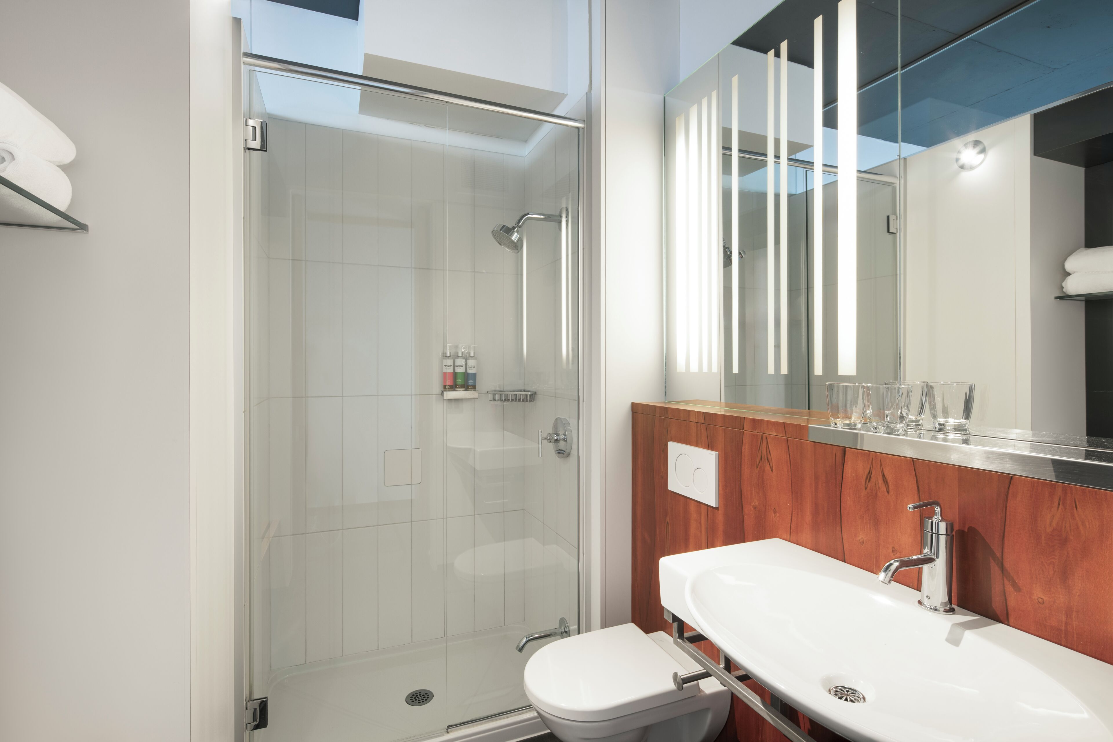 Een moderne badkamer met een douchecabine van glas, een witte wastafel en een houten opbergmeubel.
