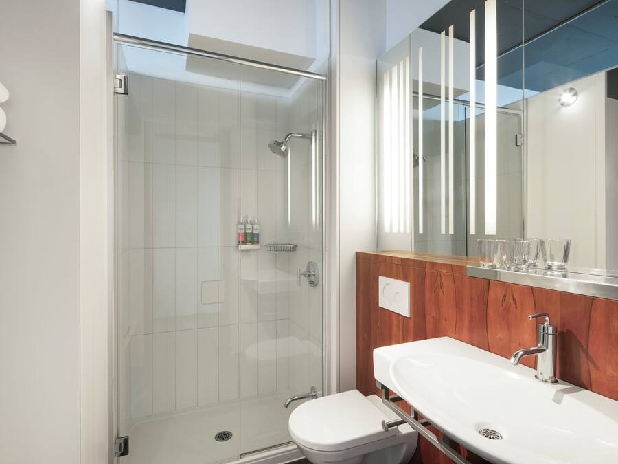 A modern bathroom with a glass-enclosed shower, a white sink, and a wooden vanity.