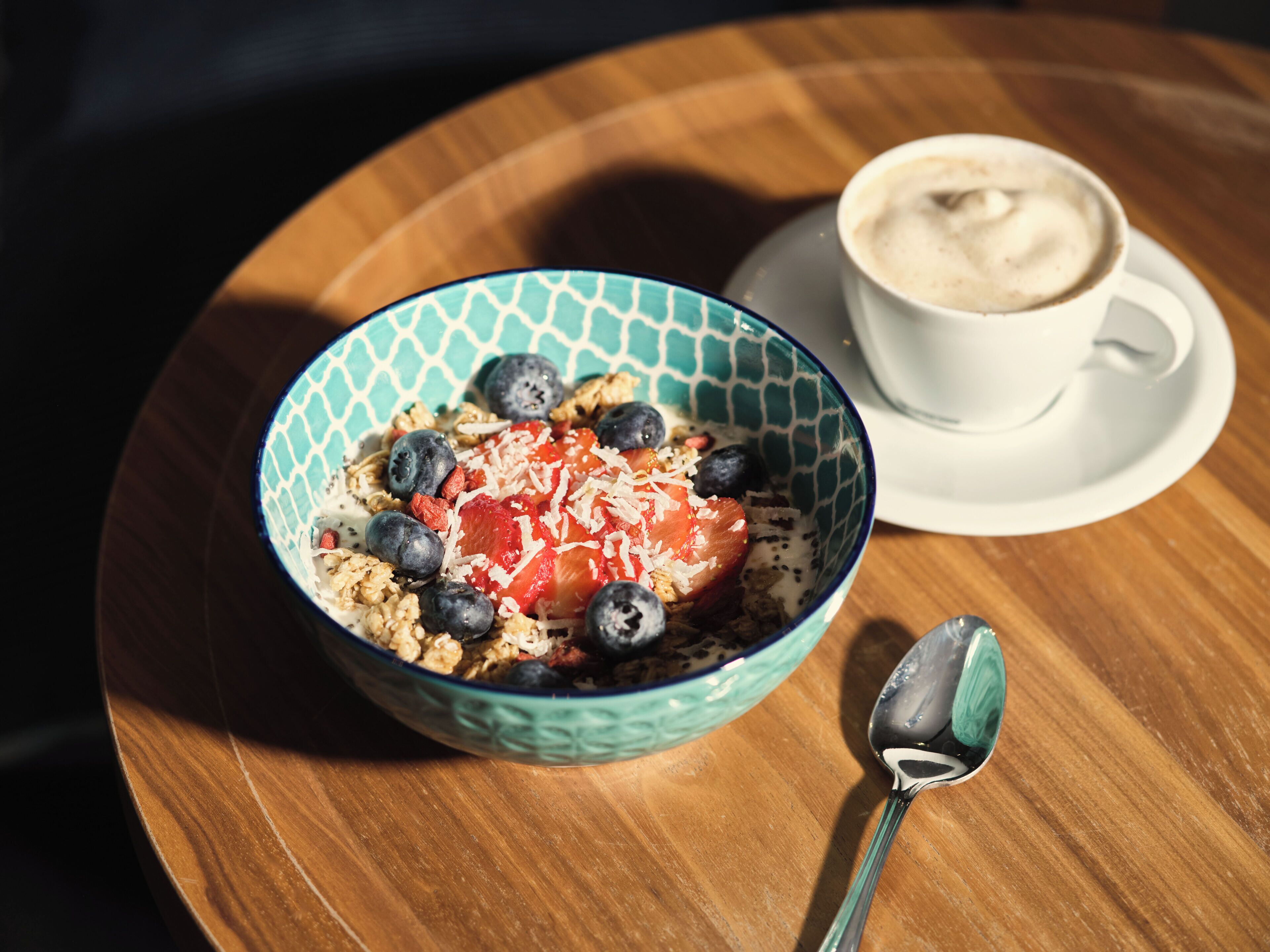 Un bol de cereals amb fruita i una tassa de cafè damunt d'una taula de fusta.