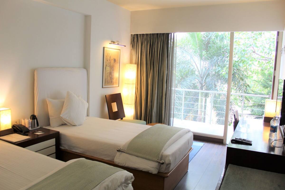 A hotel room with two beds, a desk with a lamp, a phone, and a window with curtains.