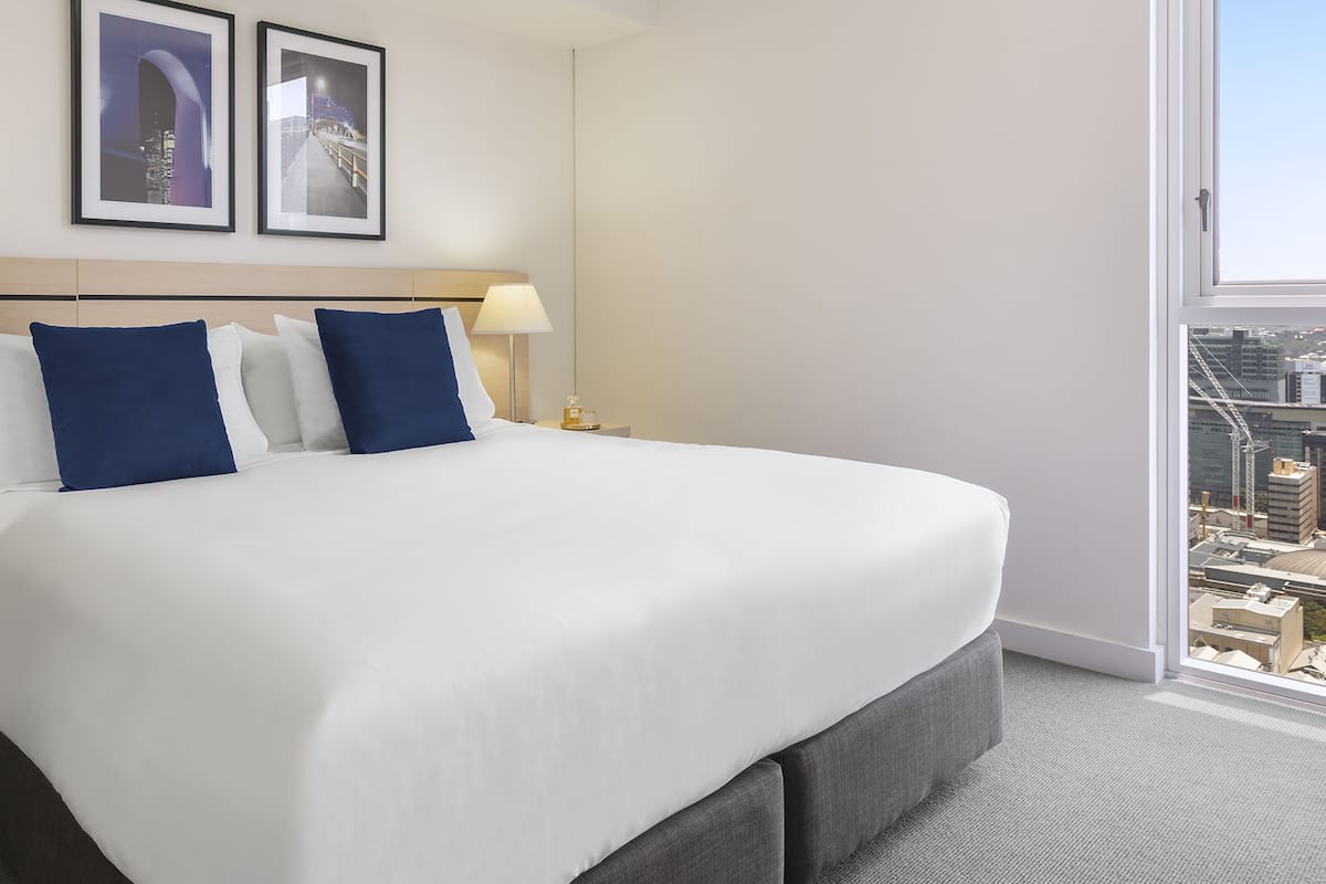 Ein Hotelzimmer mit einem großen Bett, einem Nachttisch, einer Lampe und zwei gerahmten Bildern an der Wand.