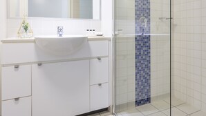 Une salle de bain avec un lavabo blanc, une cabine de douche en verre et un miroir au-dessus du lavabo.