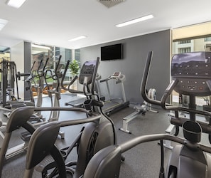 A gym with various exercise equipment, a large mirror, and a TV on the wall.