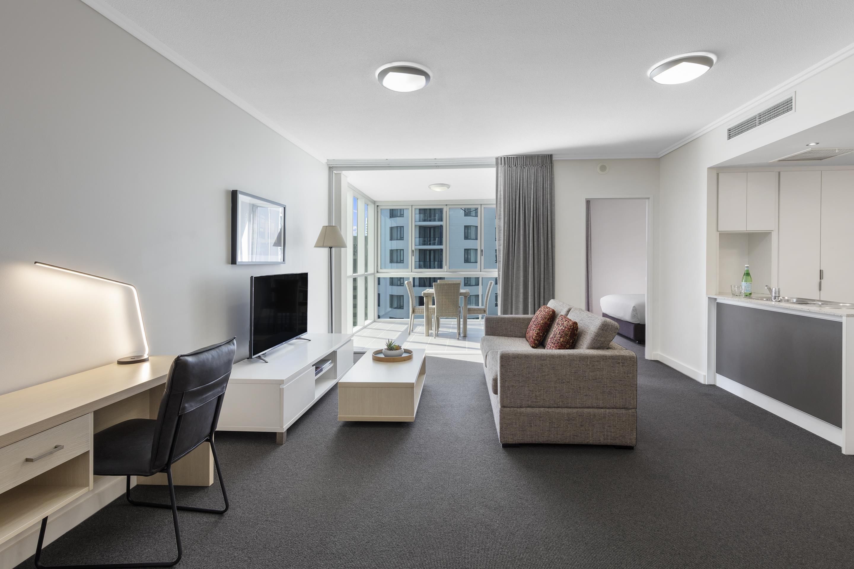 A modern hotel room with a flat-screen TV, a desk, a sofa, and a dining area.