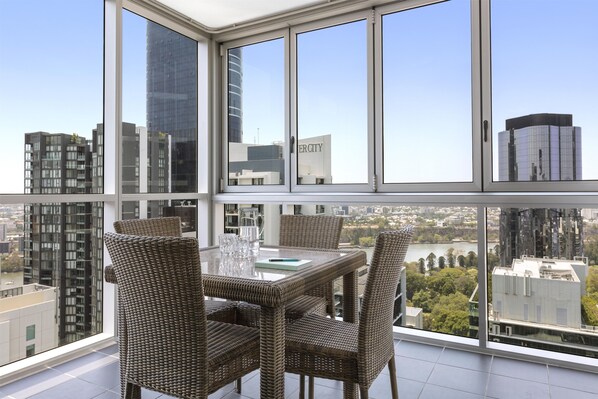 Un apartamento de altura con un balcón grande, amoblado con sillas de mimbre y una mesa, que ofrece vistas a la ciudad.
